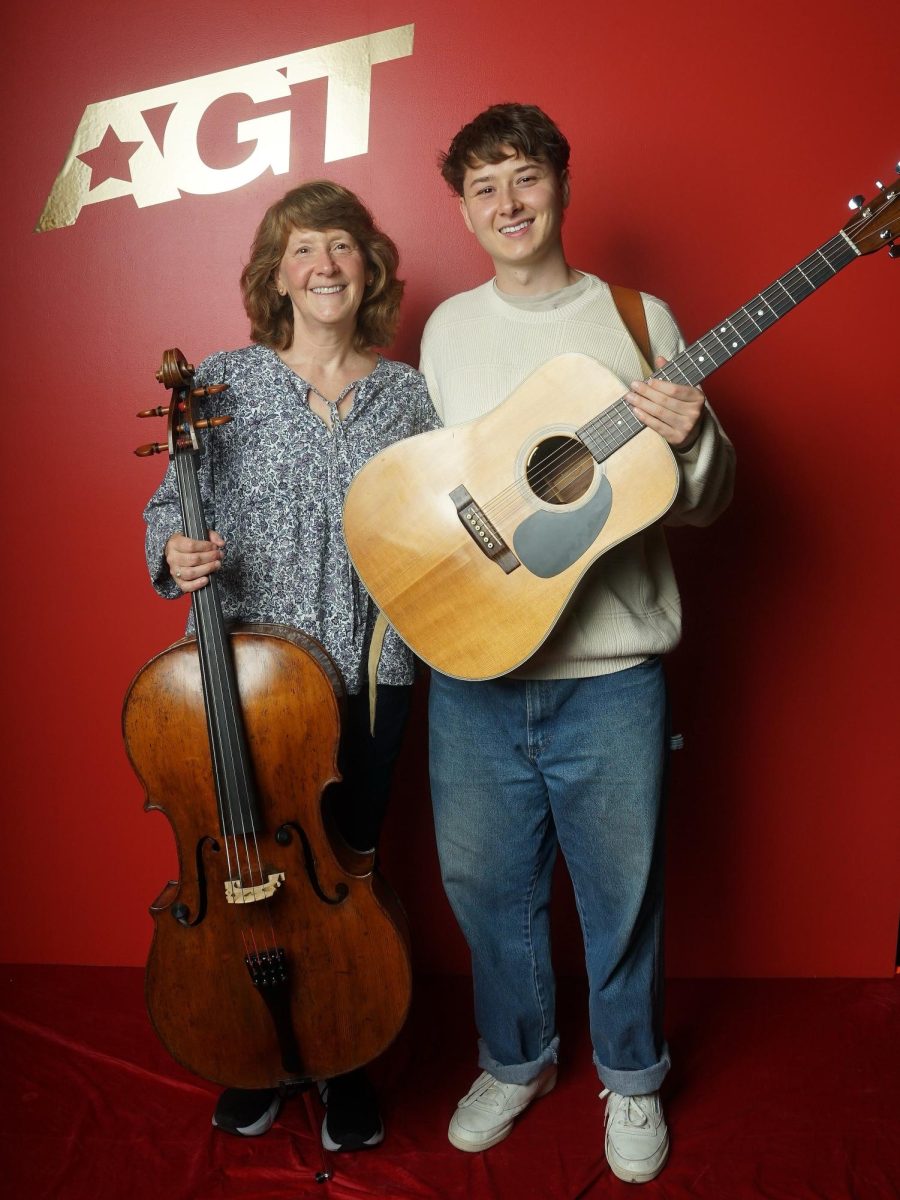 Cole and Judy Swensen posing for a photo at AGT. Cole is holding his guitar while Judy is holding her cello.